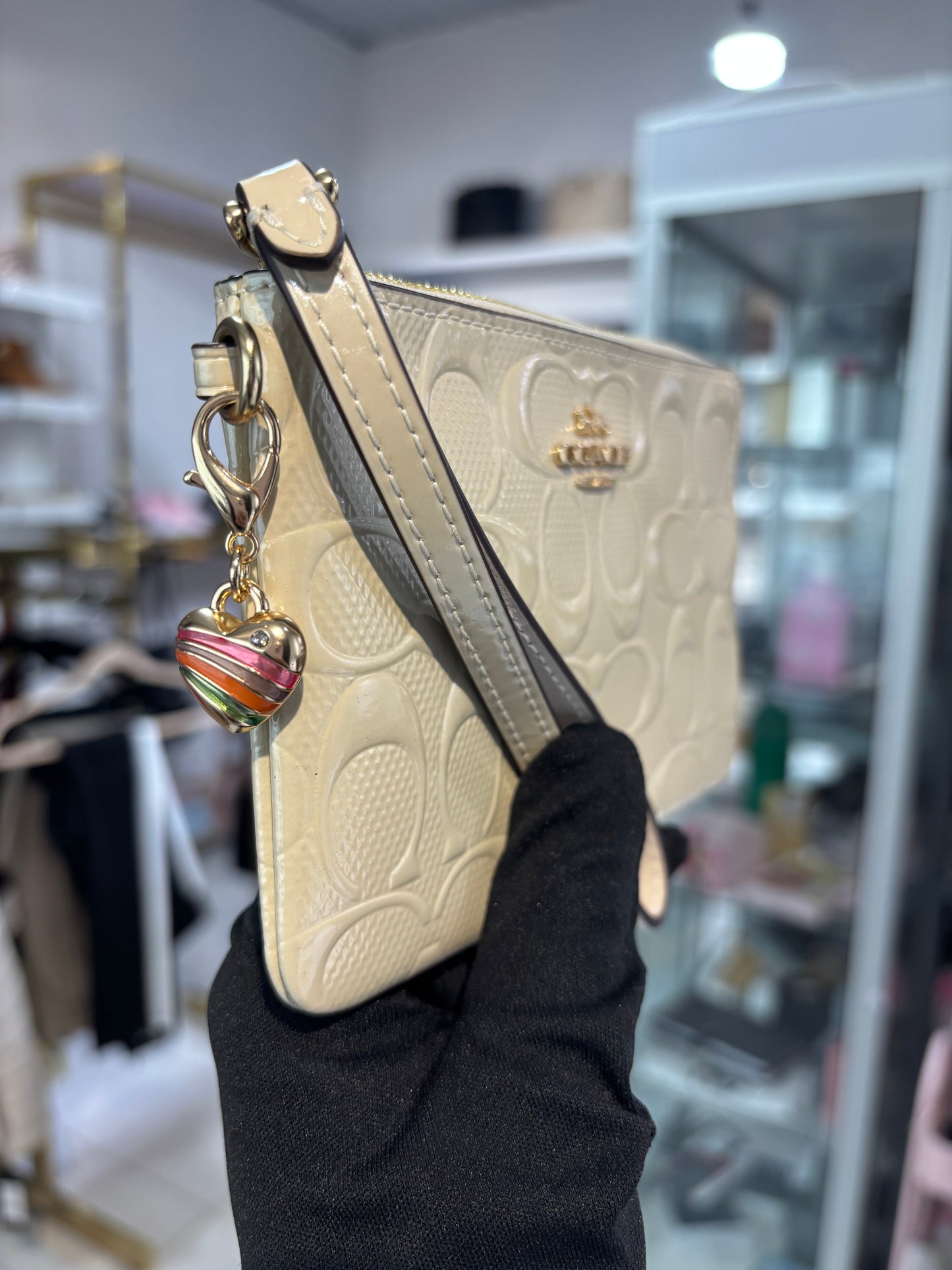 Muñequera Coach beige de charol con dije de corazón