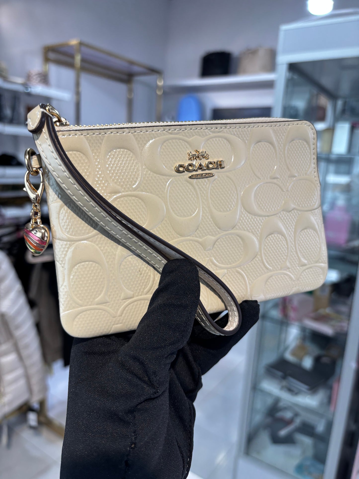 Muñequera Coach beige de charol con dije de corazón