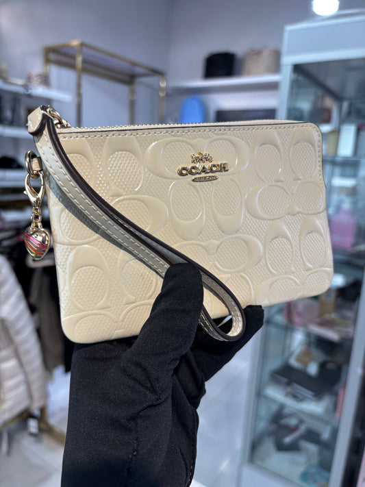Muñequera Coach beige de charol con dije de corazón